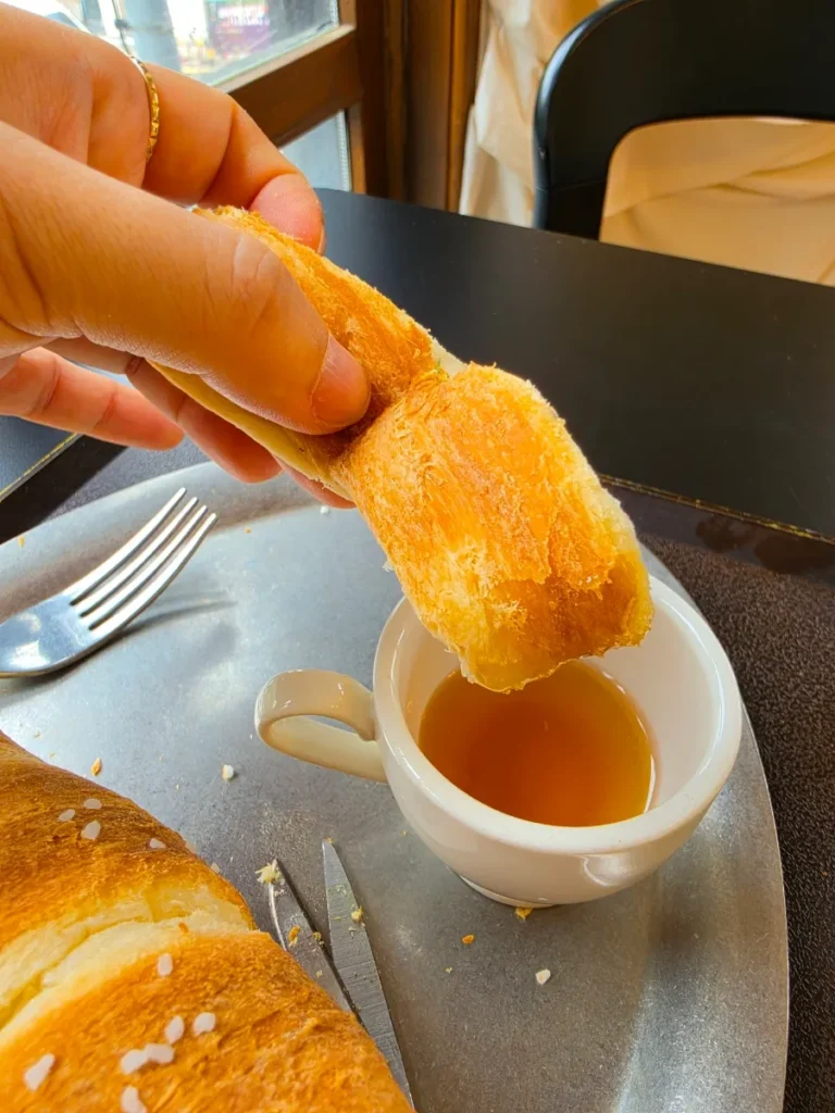 A piece of signature chimney cake held above a small cup of honey