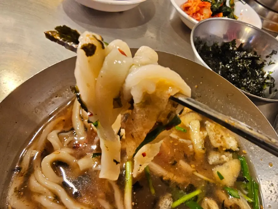 Close-up of thick handmade kalguksu noodles held with chopsticks