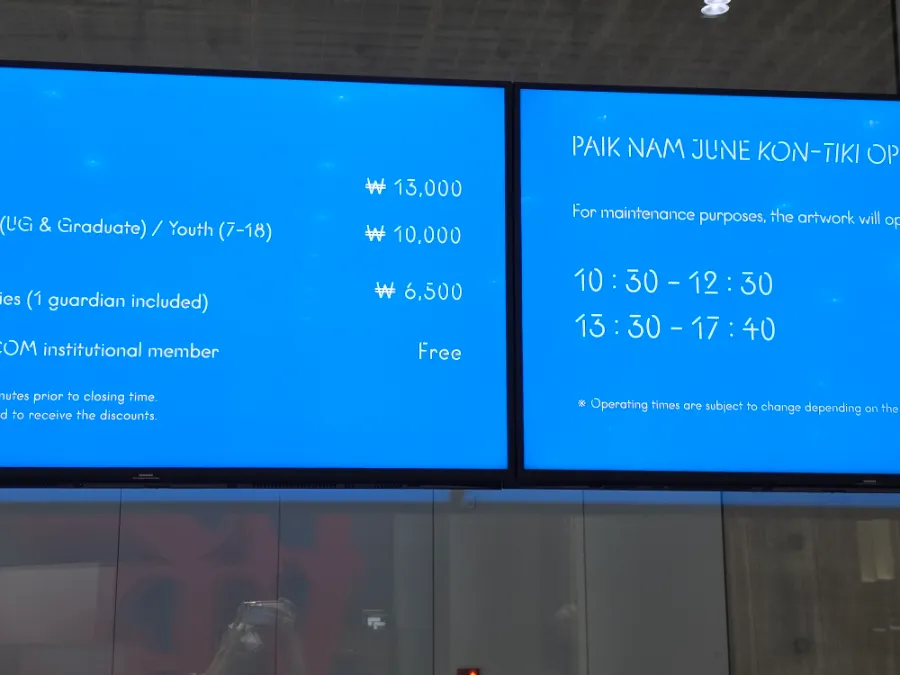 Blue information screens displaying museum admission prices and Paik Nam June artwork operating times.