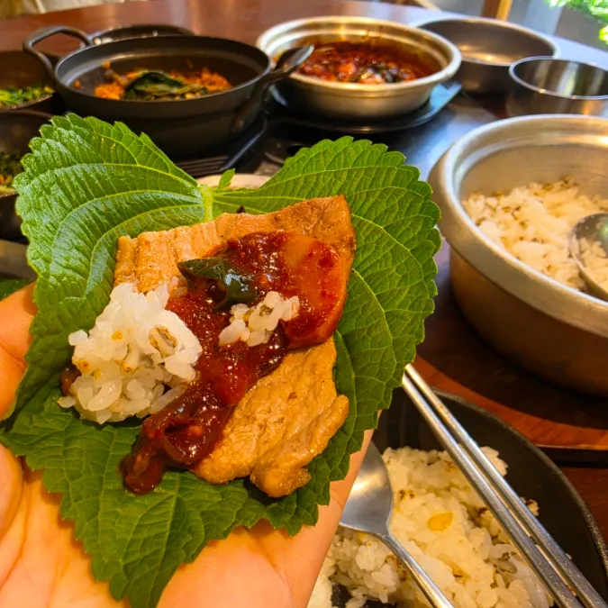Korean grilled pork wrap with rice and sauce on a perilla leaf