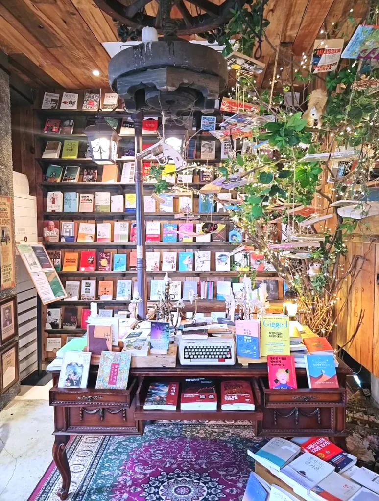 Books and a vintage typewriter displayed on a wooden desk beneath hanging decorations at Manhole Coffee Western Book Cafe in Seoul.
