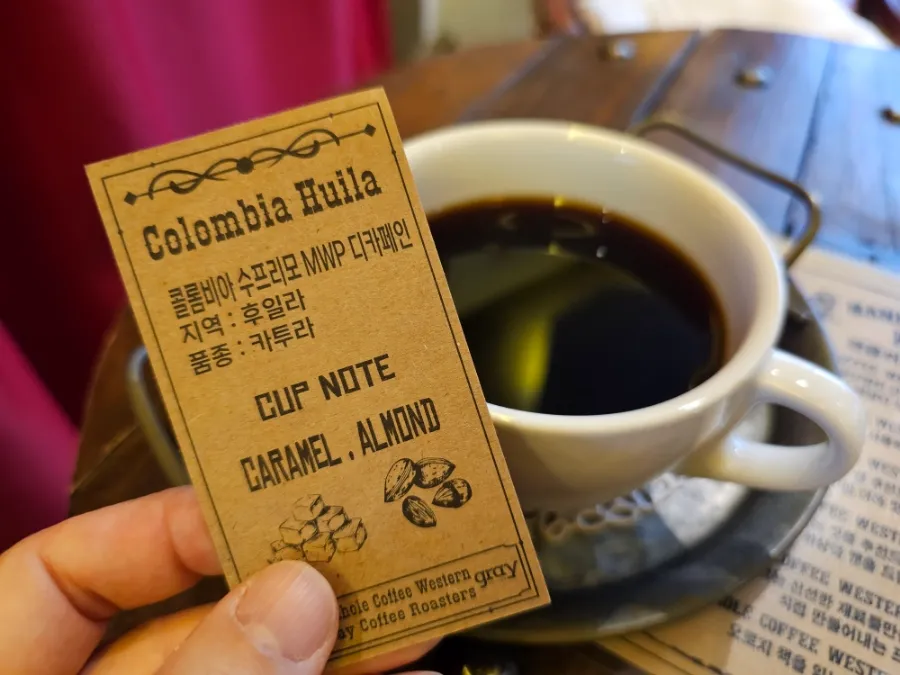 Colombia Huila decaf coffee information card held beside a cup of black coffee at Manhole Coffee Western.