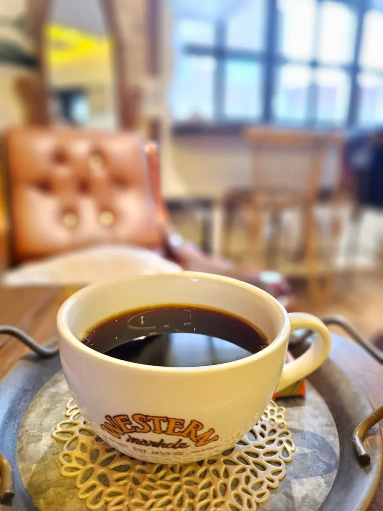 Black drip coffee in a cream-colored Western-branded cup on a tray, with vintage seating in the background.