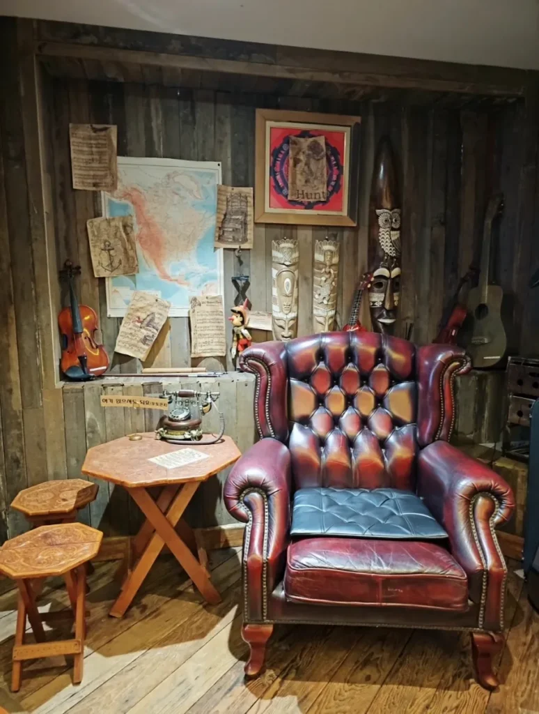Burgundy leather armchair beside a vintage telephone, musical instruments and a map in a wood-paneled cafe corner.