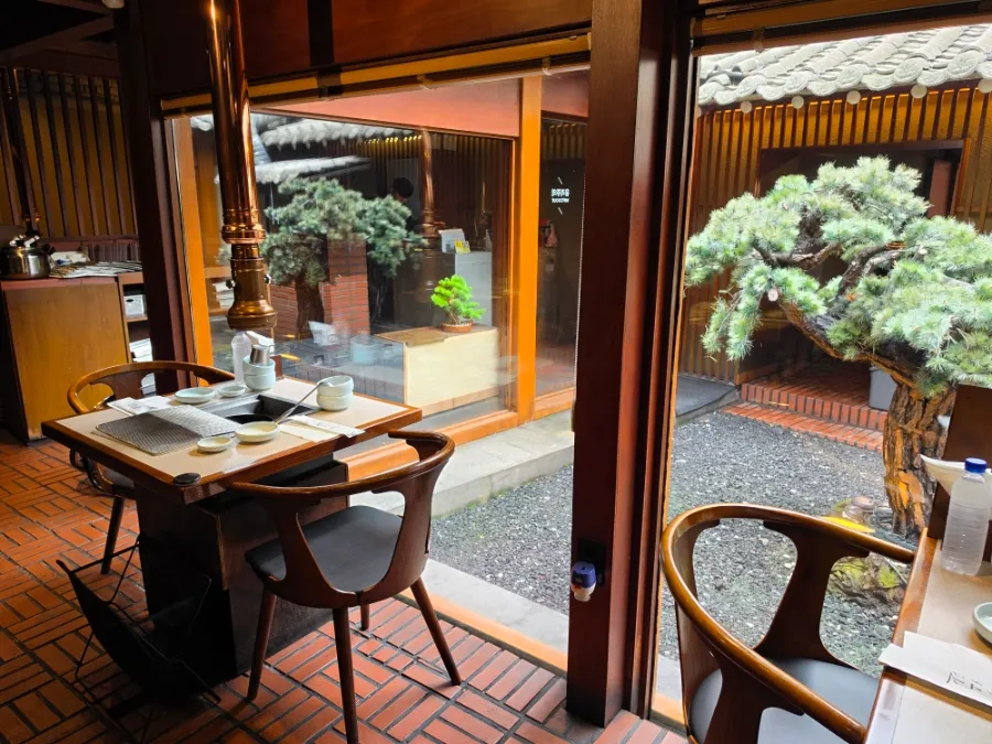 Window-side dining tables overlooking the pine-tree courtyard at Tonguidong Gukbingwan.