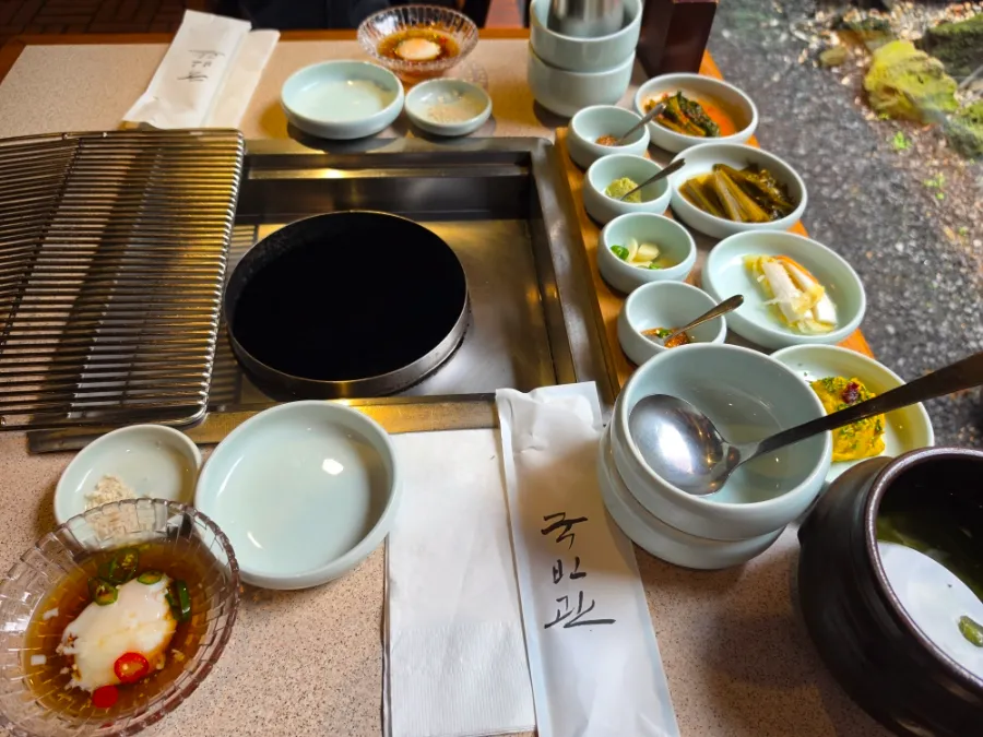 Korean side dishes and dipping sauces arranged around a tabletop grill at Tonguidong Gukbingwan.