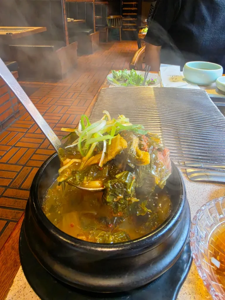 Steaming soup with leafy greens served in a black stone bowl at Tonguidong Gukbingwan.
