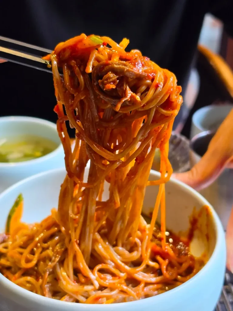 Chopsticks lifting spicy buckwheat noodles from a bowl at Tonguidong Gukbingwan.
