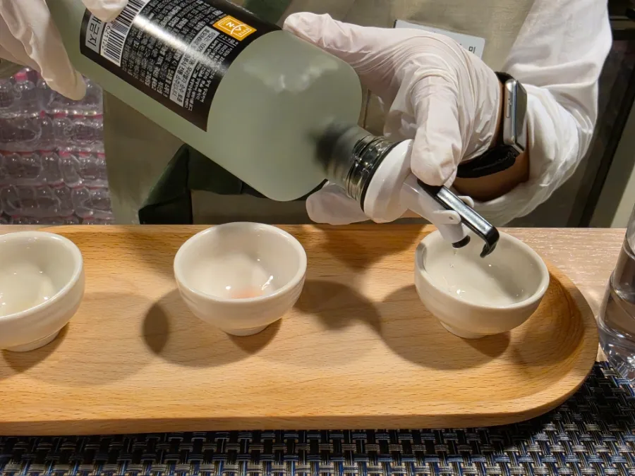 Staff member pouring Korean traditional liquor into a ceramic tasting cup during a guided tasting in Seoul