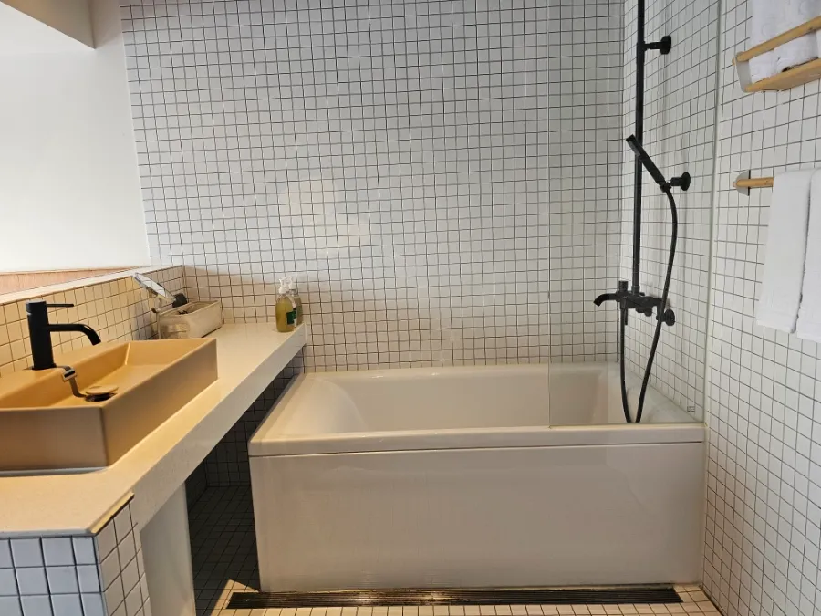 Bathtub and sink in the tiled bathing area at Local Stitch Tongyeong
